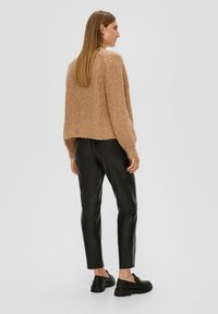 Flauschiger, hellbrauner Strickpullover mit verkürztem Saum und geripptem Muster, kombiniert mit schwarzen, eng anliegenden Lederhosen und schwarzen Plateauschuhen.