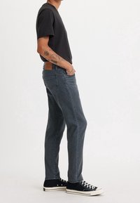 Mörkblå jeans med avslappnad passform, subtila blekningar och en brun läderlapp på baksidan. Tillsammans med en svart kortärmad skjorta och svarta sneakers.