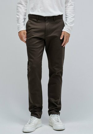 Pantalons marron foncé en tissu lisse avec une coupe ajustée, dotés d'une fermeture à boutons et de passants de ceinture, associés à des baskets blanches.
