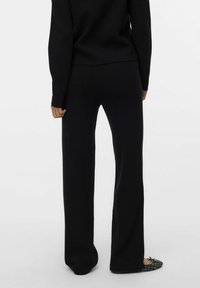 Pull en maille noire et pantalon large assorti. Texture douce avec une coupe droite, design minimaliste, et chaussures plates à motif tissé.