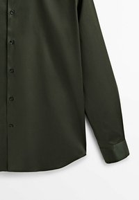 Camicetta lunga verde scuro realizzata in tessuto liscio. Presenta chiusura con bottoni, orlo arrotondato e dettagli ai polsini. Design minimalista senza motivi.
