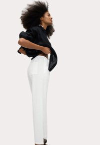 Black linen shirt with rolled sleeves, paired with white, textured wide-leg pants featuring a back pocket. Model in side profile.