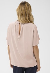Blouse à manches courtes en satin rose doux, dotée d'un détail en trou de serrure au dos et d'une coupe décontractée, avec une texture lisse et légèrement fluide.