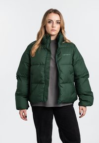 Giacca a vento verde scuro con colletto alto, chiusura con zip e polsini elasticizzati. Presenta un logo discreto sul petto e una texture trapuntata.