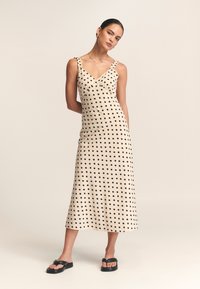 Crème-kleurige midi-jurk met zwarte stippen, met een v-hals en gerimpelde schouderbandjes. Zachte stof met een vloeiende silhouet.