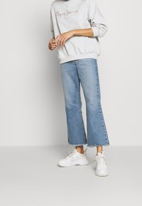 Felpa grigia con testo ricamato, jeans a vita alta blu chiaro con orlo sfilacciato e scarpe da ginnastica bianche con lacci.