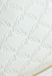 Tissu blanc texturé présentant un motif en relief de formes en boucle et de petites courbes, avec une fermeture éclair dorée le long du bord inférieur.