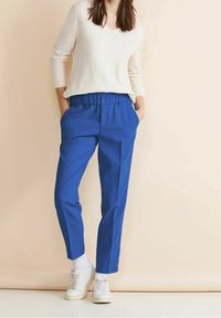 Blå, byxor med elastisk midja och avslappnad passform, med två sidofickor. Toppad med en ljusfärgad, långärmad stickad tröja och vita sneakers.