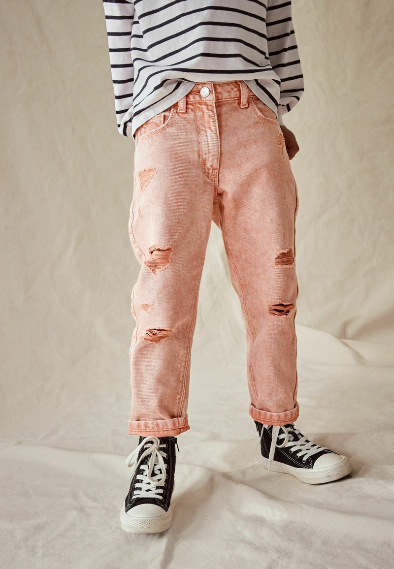 Abbigliamento per bambini con jeans strappati rosa, sneakers alte nere con lacci bianchi e una maglietta bianca a maniche lunghe con strisce orizzontali nere.