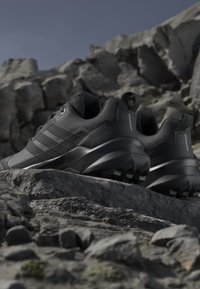 Chaussures de randonnée noires avec semelles robustes posées sur un terrain rocheux sous un ciel dégagé.