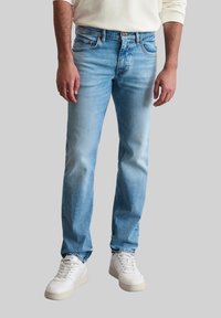 Jean en denim bleu clair avec une coupe droite, design à cinq poches et décoloration subtile. Associé à des baskets blanches.