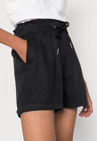 Shorts noirs avec une taille élastique, un cordon de serrage ajustable, deux poches latérales et des ourlets retroussés. Le tissu semble doux et léger.
