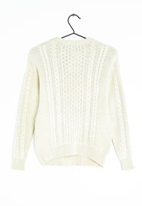 Krémový svetr s copánkovým vzorem a dlouhými rukávy zavěšený na černém ramínku proti bílému pozadí.