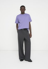 Paarse katoenen t-shirt gecombineerd met grijze, hooggetailleerde, wijd uitlopende broek. Afgewerkt met een zwarte riem en zwarte schoenen. Eenvoudig ontwerp en stoftextuur.