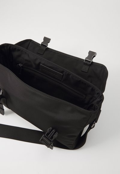Geantă de umăr din nylon negru cu un design elegant, având un capac frontal, două închideri tip clips și un buzunar interior cu fermoar. Curea ajustabilă inclusă.