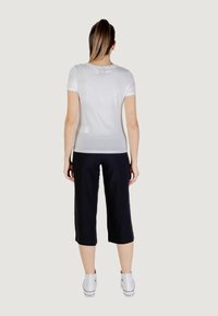 Camiseta blanca ajustada de manga corta, combinada con pantalones negros cortos y zapatillas blancas. Diseño simple, tejido suave y sin estampados.