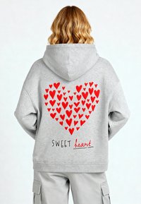 Felpa grigia con un grande cuore rosso composto da cuori più piccoli sulla schiena, accompagnato dal testo "SWEET heart" in nero sottostante.