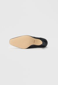 Scarpa in pelle nera con punta affusolata, texture liscia e suola marrone chiaro. Presenta un design a taglio basso e un profilo minimalista.
