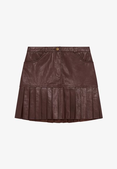 Bruine leren plissérok met een hoge taille, voorzien van twee voorzakken en een gouden knoop bij de tailleband. Plissé's lopen uit vanaf de zoom.