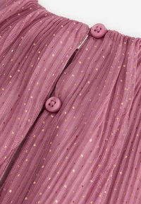 Tissu en tulle rose à pois dorés, doté d'un design froncé et de deux boutons roses au niveau du col, créant une apparence texturée et superposée.