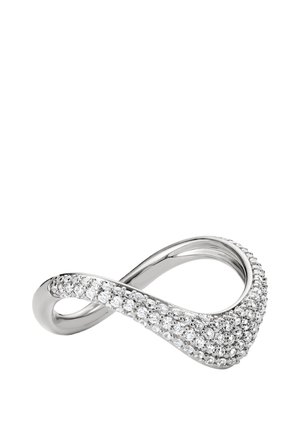 Silberner Ring in Form eines Unendlichkeitssymbols, eine Seite mit kleinen runden funkelnden Diamanten besetzt, vor weißem Hintergrund.