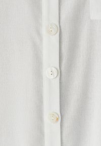 Bela lanena tkanina z gumbno letvico in okroglimi gumbi iz morskega bisera. Tekstura je lahka in rahlo teksturirana.