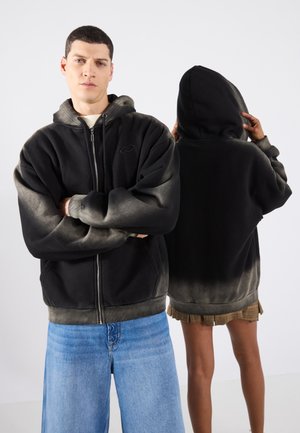 Felpa nera con zip e sfumatura grigia, dotata di tasca frontale e cappuccio con cordini. Modelli presentati frontalmente e posteriormente, indossando jeans blu.