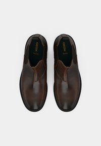 Brown leather slip-on shoes with a smooth finish, rounded toe, elastic side panels, and contrasting black rubber sole. Brand logo visible inside.