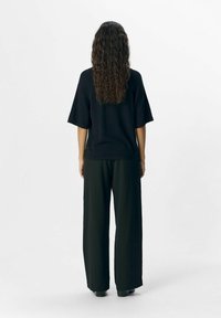 Black oversized t-shirt with short sleeves, paired with loose black trousers. Textured fabric, simple design, and straight silhouette.