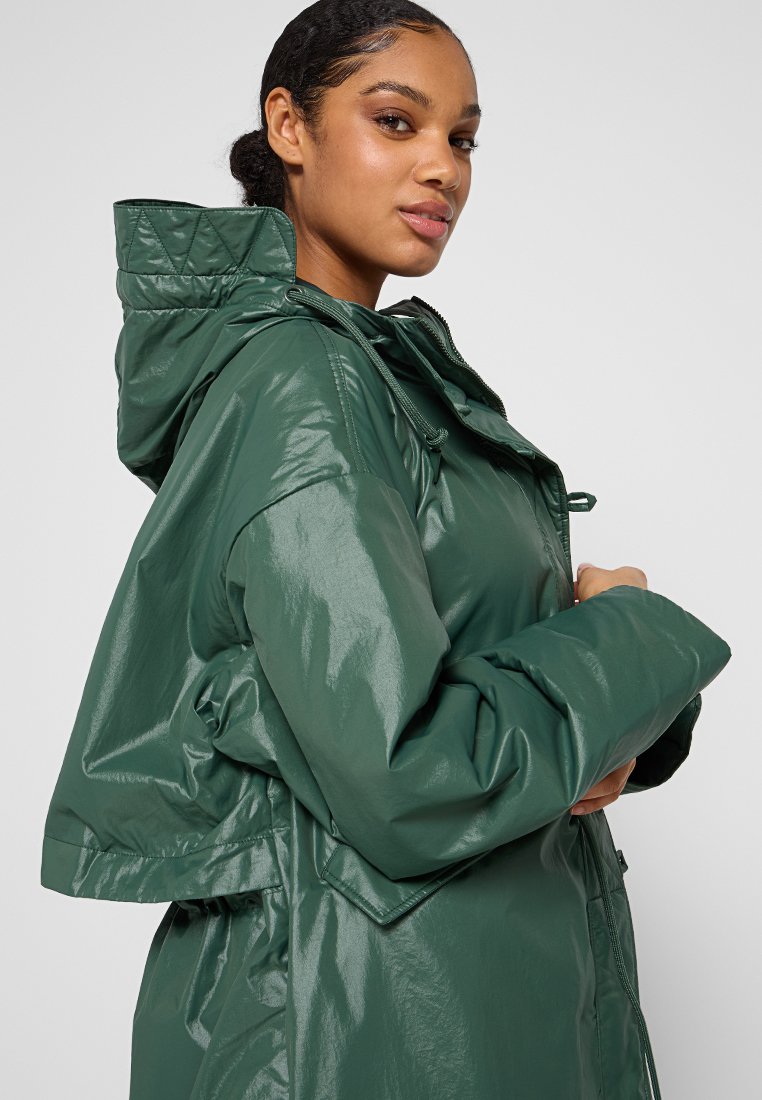 Chaqueta verde, brillante, con capucha y cuello acolchado, de corte holgado y cordones elásticos. Presenta un acabado texturizado y brillante, además de grandes bolsillos.