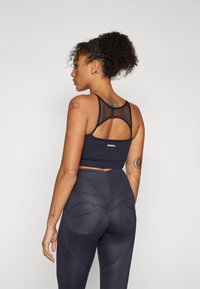 Top corto atlético negro con espalda de malla, combinado con leggings de cintura alta que presentan detalles de costura curvada y acentos de bolsillo.
