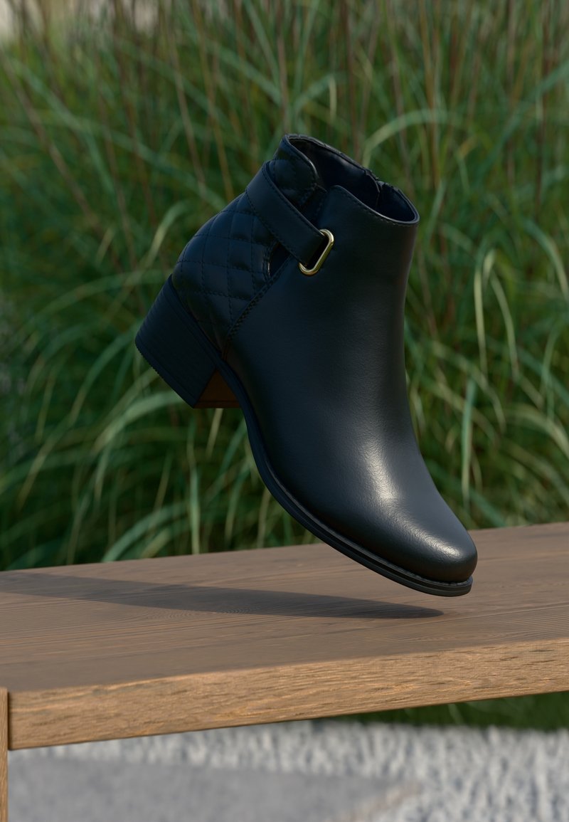 Bottine en cuir noir avec dos matelassé et boucle dorée, flottant au-dessus d'un banc en bois en extérieur avec un fond d'herbe verte.
