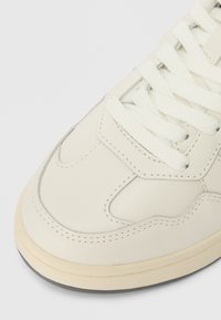 Hvide lædersneakers med strukturerede overflader, tykke snørebånd og en gummisål med en kontrasterende tan trim og sorte såle accenter.