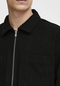 Black wool blend jacket featuring a pointed collar, front zipper, and two patch pockets with a brushed texture.