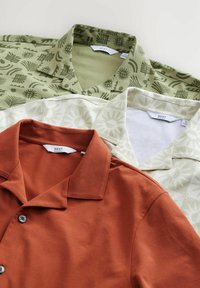 Tre skjorte med krave: en orange ensfarvet skjorte, en grøn mønstret skjorte med abstrakte designs, og en hvid skjorte med solmotiver.