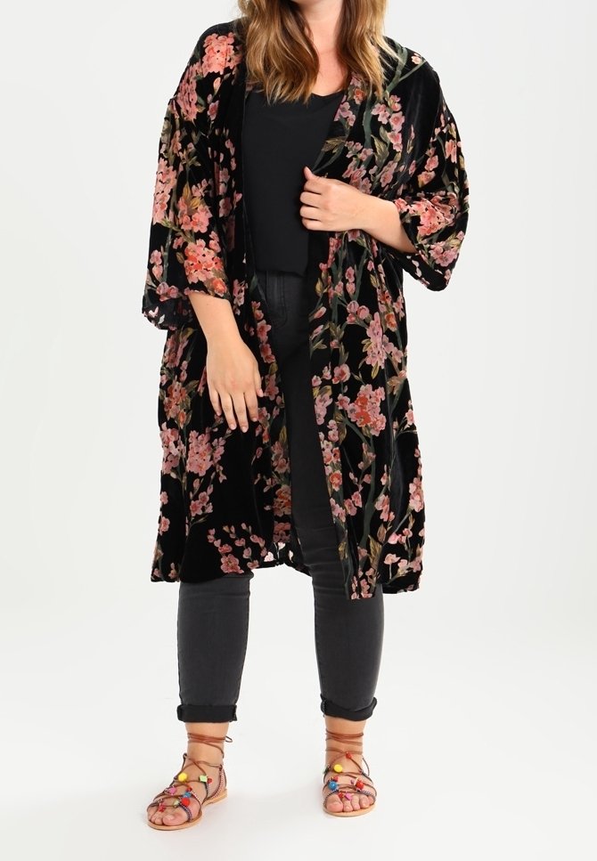 Black velvet kimono with floral pattern, featuring loose sleeves and an open front design. Worn over a black top and paired with dark jeans and sandals.