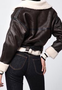 Brun läderjacka med fårskinnskrage och manschetter, med en kortad design och bältesdetalj, i kombination med mörka denimjeans.