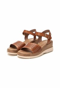 Sandalias de cuero marrón con un diseño perforado, correa ajustable en el tobillo y suela de goma beige. Con un tacón en cuña para mayor altura.