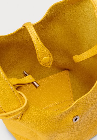 Žuta kožna torba s teksturiranim završetkom, s glatkom unutrašnjosti, dva remena i magnetskim zatvaračem.