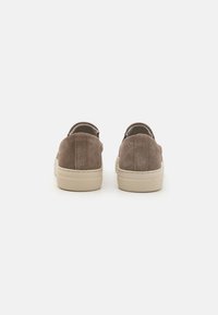 Zapatos de ante marrón tipo slip-on con talones redondeados, suelas de goma crema y diseño minimalista. Superficie texturizada con un sutil detalle de costura.