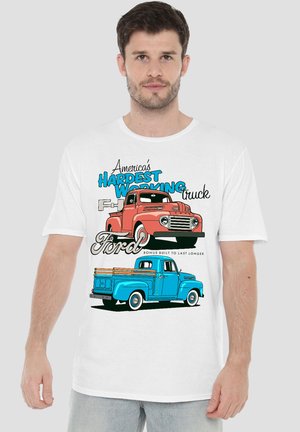 Man wearing white t-shirt with graphic of red and blue vintage Ford trucks and text "America's Hardest Working Truck Ford".