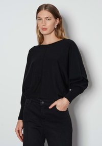 Maglia nera a maglia con scollo a barca, spalle basse e maniche lunghe. Abbinata a jeans neri a vita alta con tasca frontale.