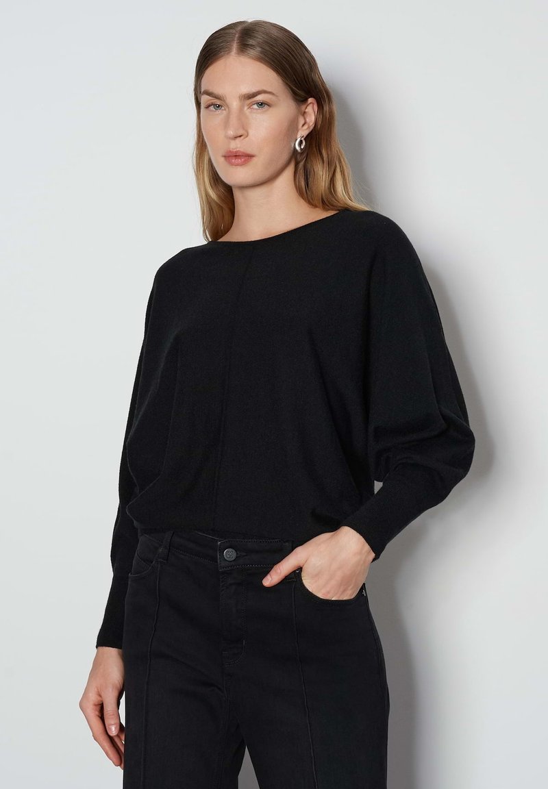 Maglia nera a maglia con scollo a barca, spalle basse e maniche lunghe. Abbinata a jeans neri a vita alta con tasca frontale.