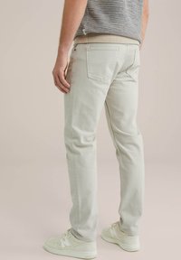 Pantalones de algodón gris claro con un corte slim, que cuentan con dos bolsillos traseros y detalles de costura sutiles, combinados con zapatillas de deporte blanco roto.