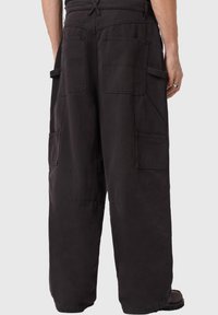 Μαύροι cargo παντελόνια με χαλαρή εφαρμογή, διαθέτουν πολλαπλές τσέπες και κορδόνι στη μέση. Το ύφασμα φαίνεται ανθεκτικό με λεία υφή.