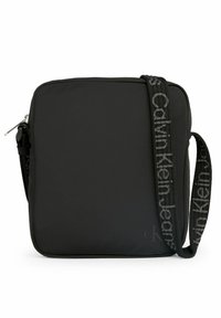 Borsa a tracolla in nylon nero con forma quadrata, chiusura con zip e una tracolla decorata con il logo "Calvin Klein Jeans".