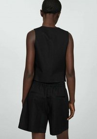 Svart avkortad topp och lösa shorts-set. Tyget är mjukt, med resårmidja och sidofickor. Enkelt mönster utan synliga mönster.