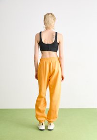 Top corto negro y pantalones de chándal naranjas holgados con puños elásticos, combinados con zapatillas blancas y grises. Modelo visto desde la espalda.
