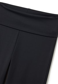 Zwarte leggings van rekbaar materiaal met een brede tailleband en minimale naden. Gladde textuur met een nauwsluitende pasvorm en geen zichtbare patronen.