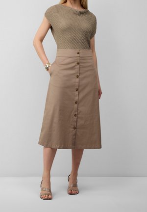Stickad topp i ljusbrun med texturfinish, tillsammans med en knä-lång beige kjol som har guldknappar och sidofickor.